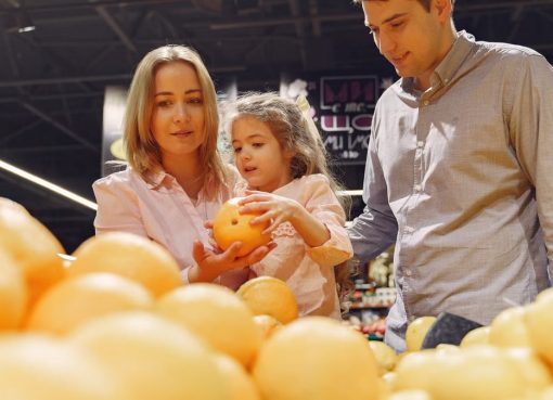 Parents and child selecting fresh oranges together at the supermarket. Captures family bonding and healthy shopping.