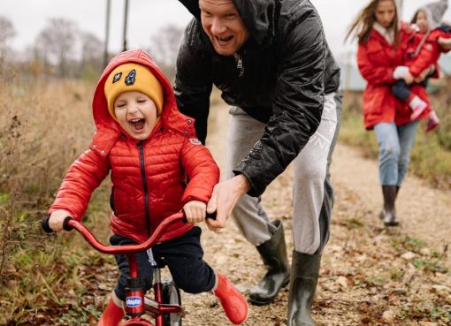 Father helping son ride a bicycle on a fall day while mother and daughter watch.